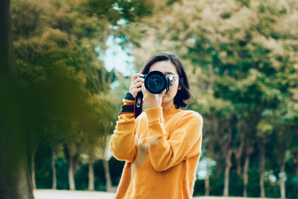 A professional wedding photographers professional wearing a yellow sweater, holding a Canon DSLR camera to capture a shot outdoors